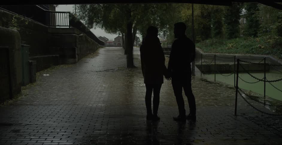 Two people stand and hold hands while it rains