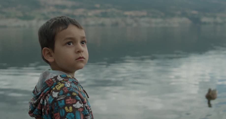 Child stands near water looking up
