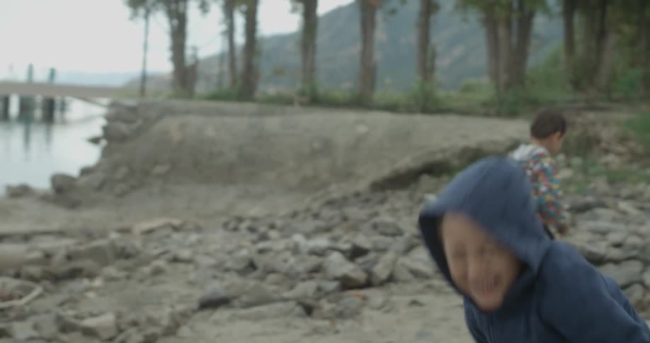A boy throws a large rock towards the water