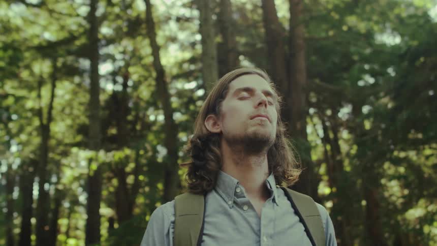 A man is standing in the forest with his eyes closed