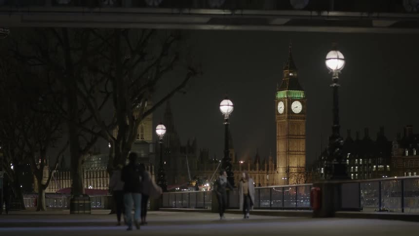 A bunch of people are walking along a pathway with big ben behind them