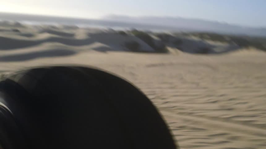 A dune buggy's tire bumps up as it drives over sand