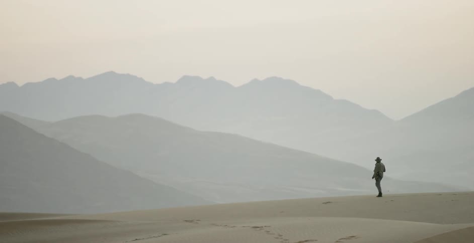 A photographer walks in a desert at sunset