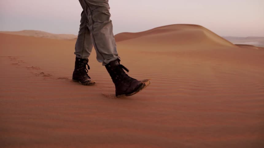 A photographer walks in a sandy desert at sunset