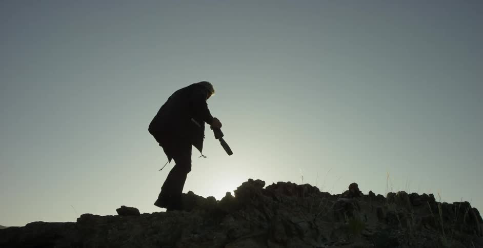 A man is climbing up some rocks at sunset