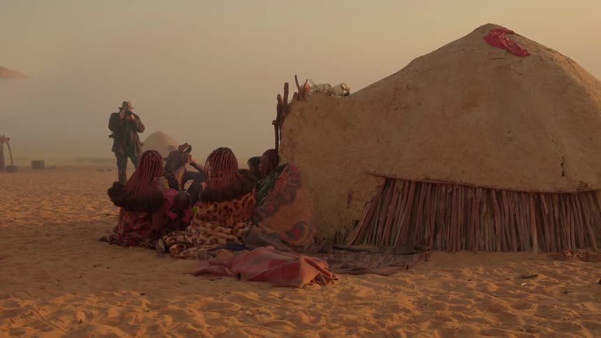 A man is photographing people living near a hut