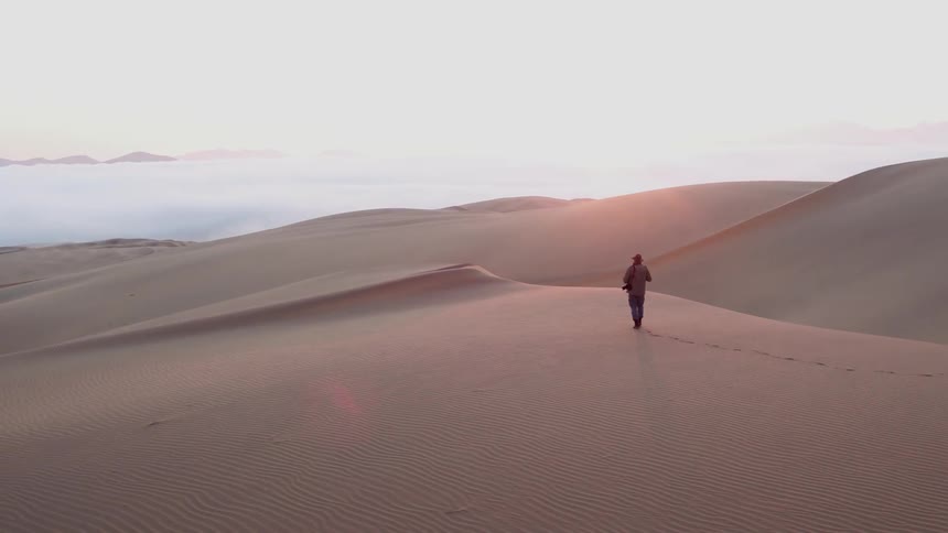 A man is hiking in the sand leaving footprints behind