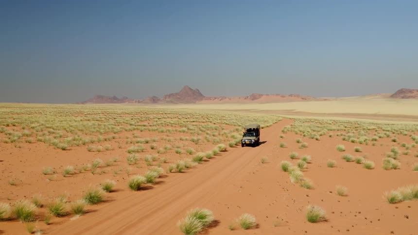 A car is driving down the dirt road in this desert