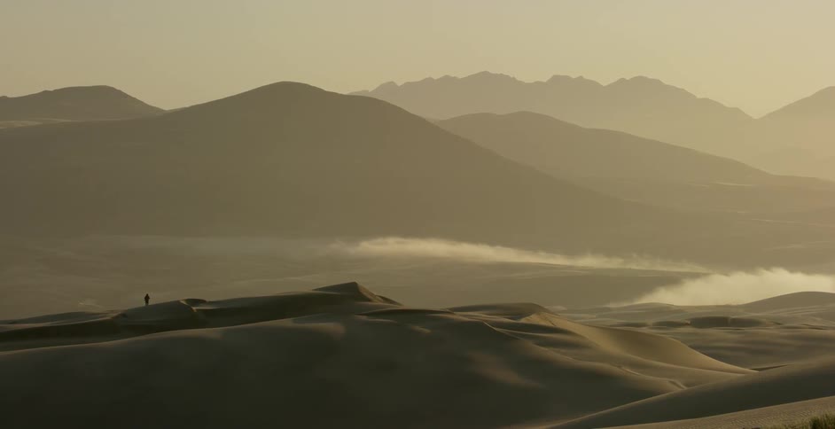 A person is hiking near the dunes in the far distance