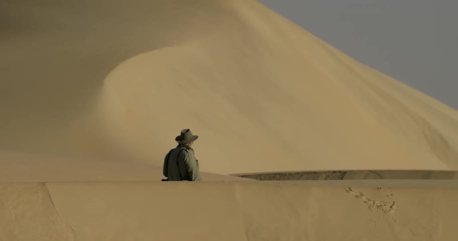 A photographer walks in the desert on a sunny day
