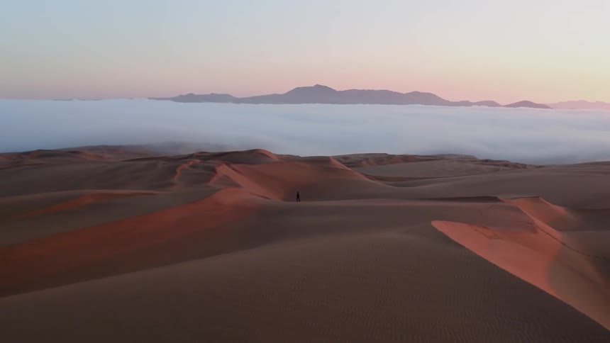 A man is walking along the desert sand dunes