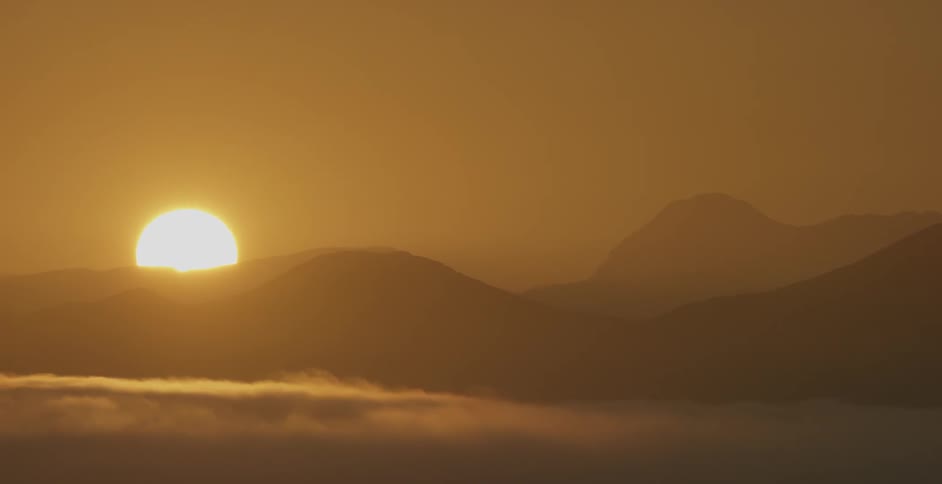 The sun sets behind the mountains ahead