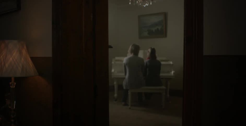 Two ladies are sitting down at a piano