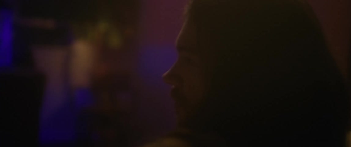 A man with long hair is sitting on a couch looking at a fish tank