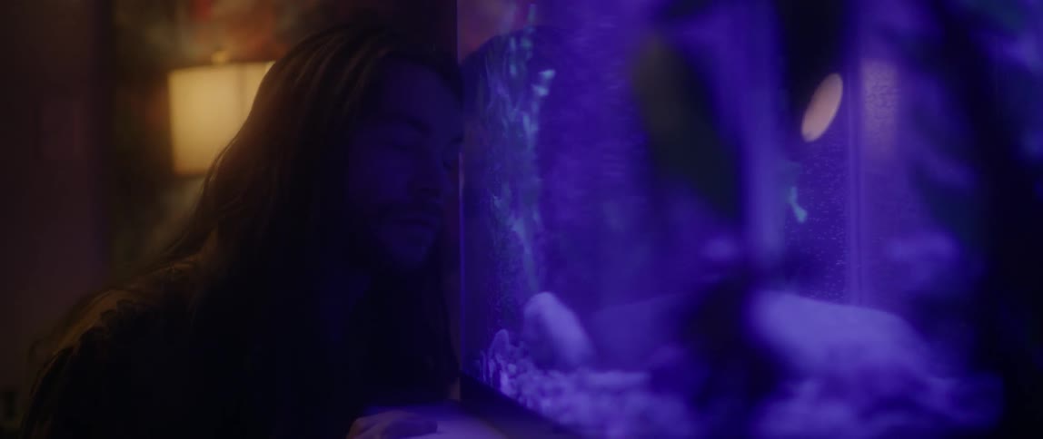 Man with long  hair rests his head against an aquarium