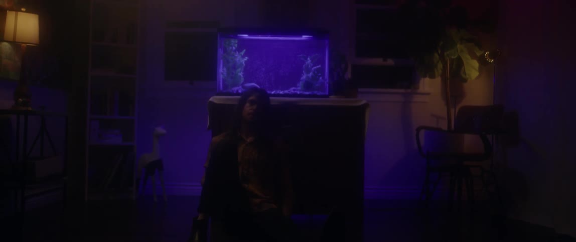 A man sits on the floor next to a fish tank in a dark room