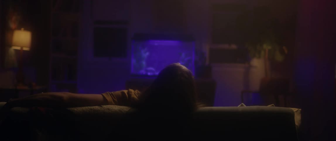 A man leans back in the couch in front of an aquarium