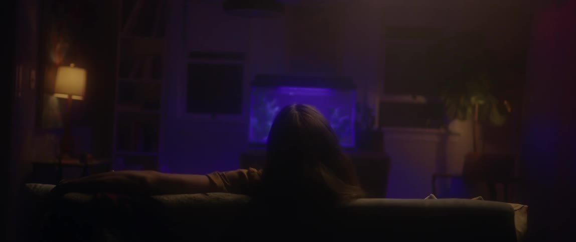 A man sits on a couch in front of a glowing fish tank