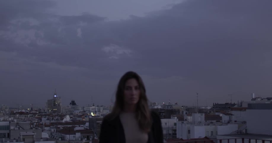 Woman  stands outside on a cloudy night with a city in the background