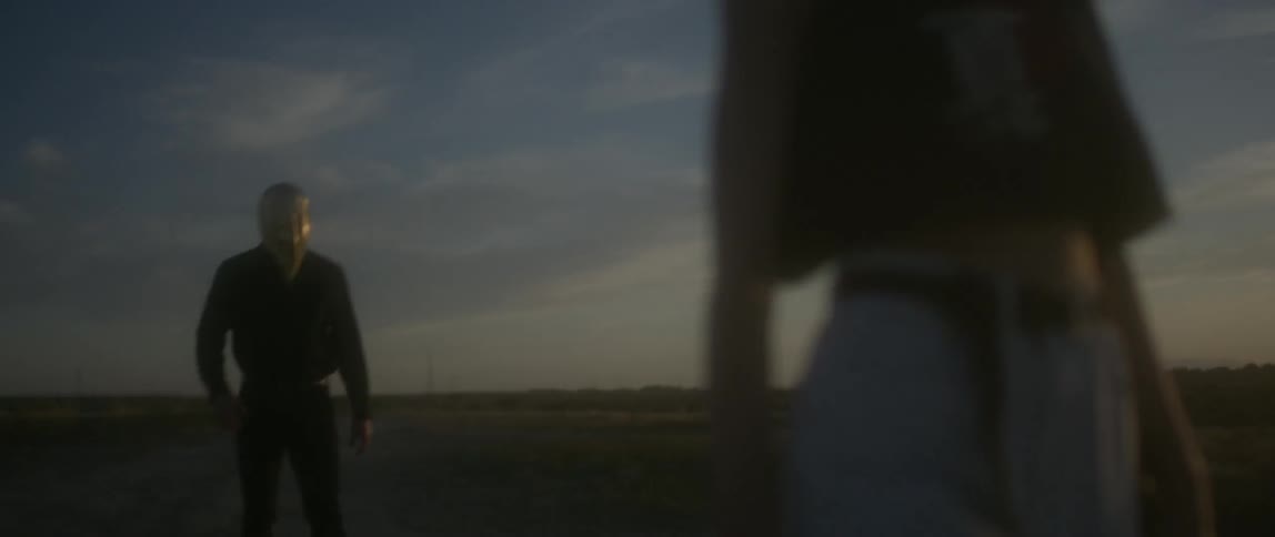 A woman is being chased down a field by hooded person