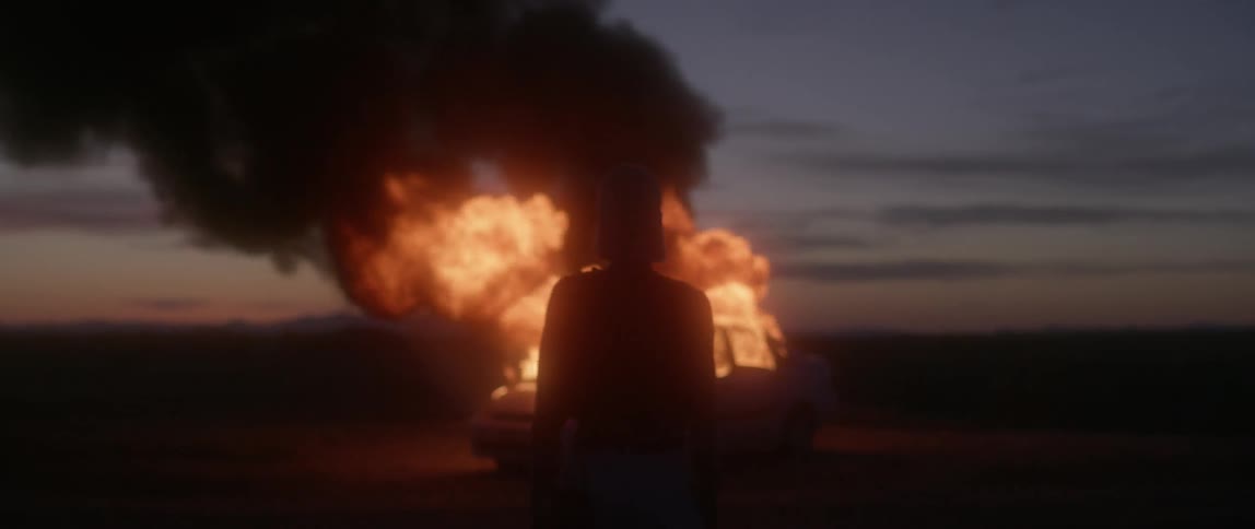 A woman watches the burning car give off smoke