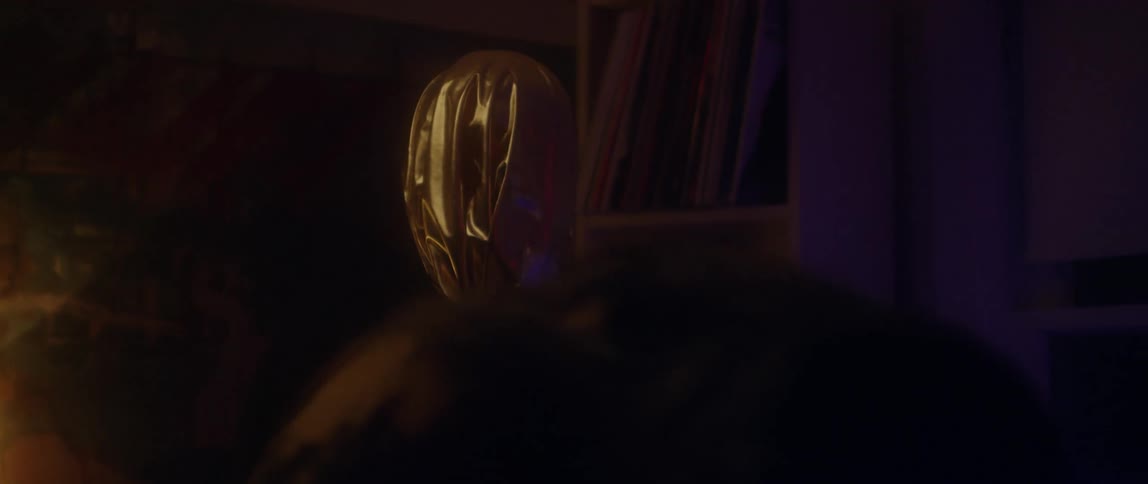 A man submerges his face in a fish tank while a masked figure stands nearby
