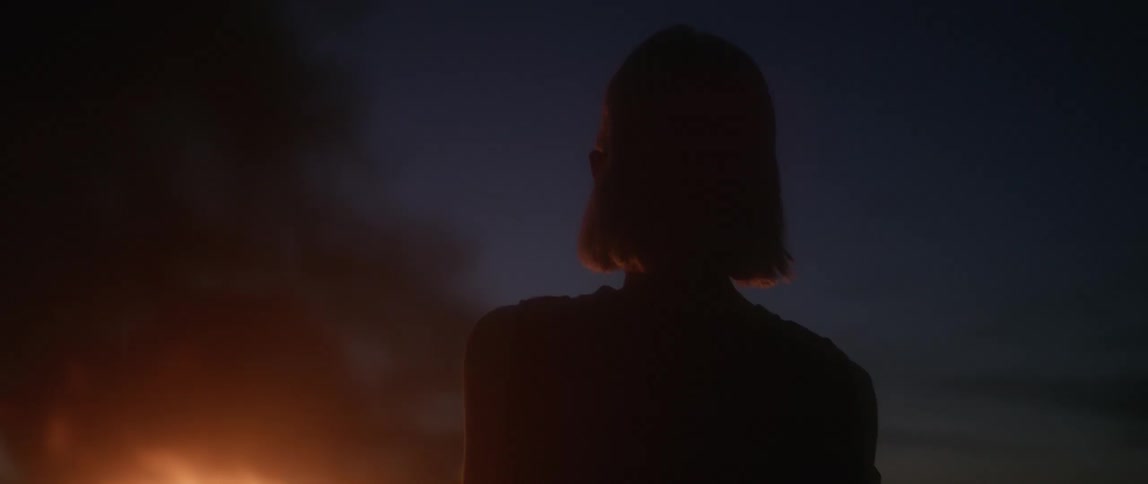 A woman stands outside watching a fire burn