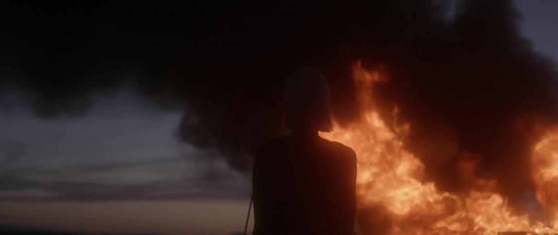 A woman watches a car burn at dusk