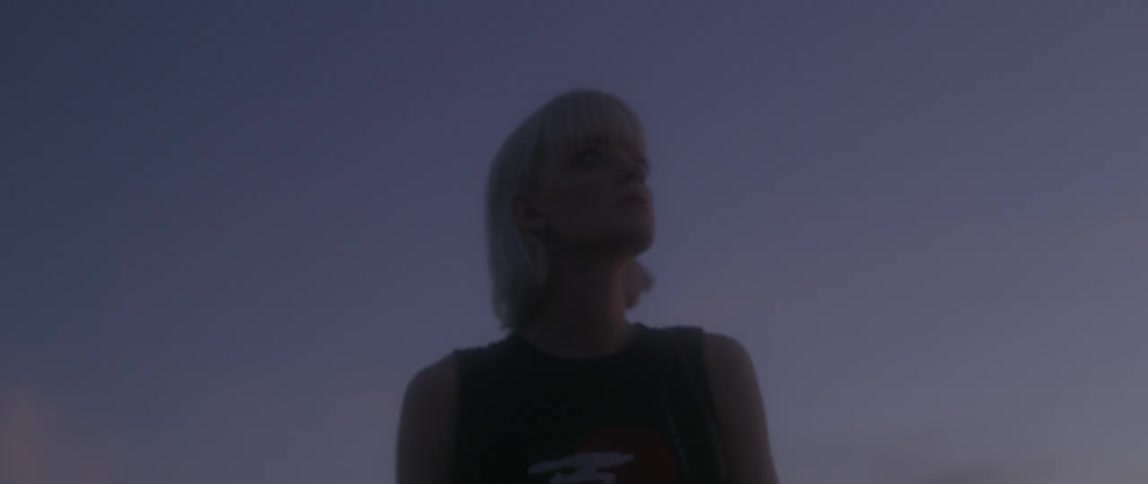 Blond woman in a sleeveless top looks off into the distance