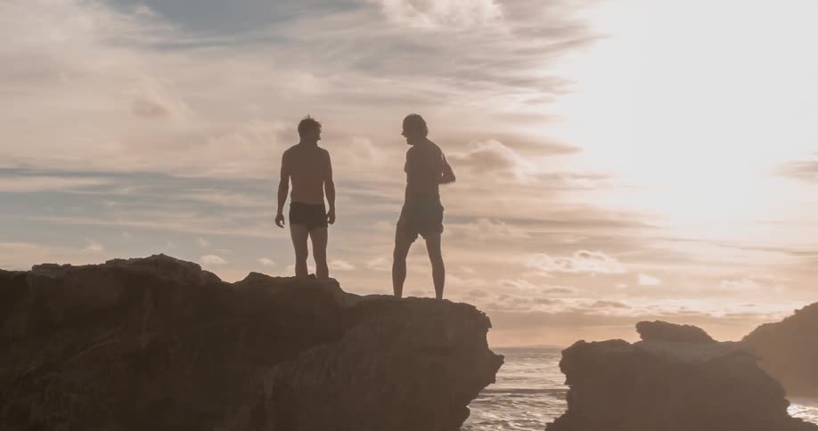Two people are standing on the rocks over the water