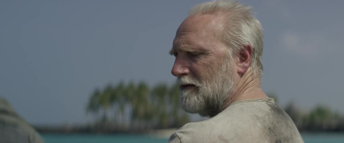 A man in a dirty shirt is looking out over the clear blue water