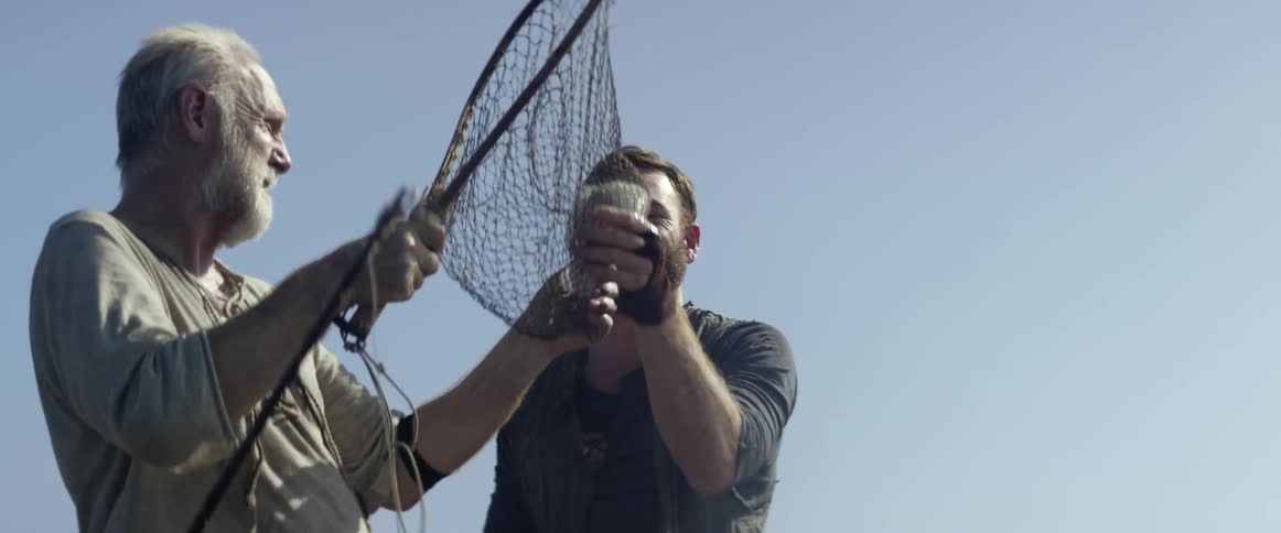 Two men look at a fish they caught in a net