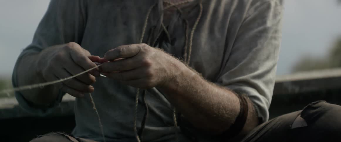 A man threads a thin rope through hooks