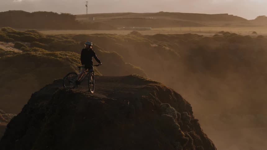 A bicyclist stands on a rocky mountain at sunset