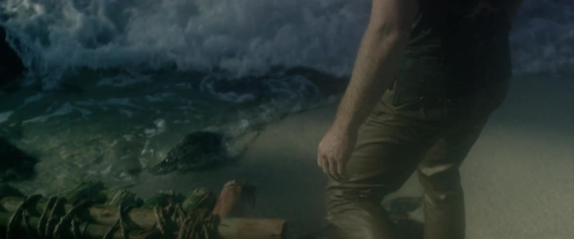A man stands by a wood raft on a beach