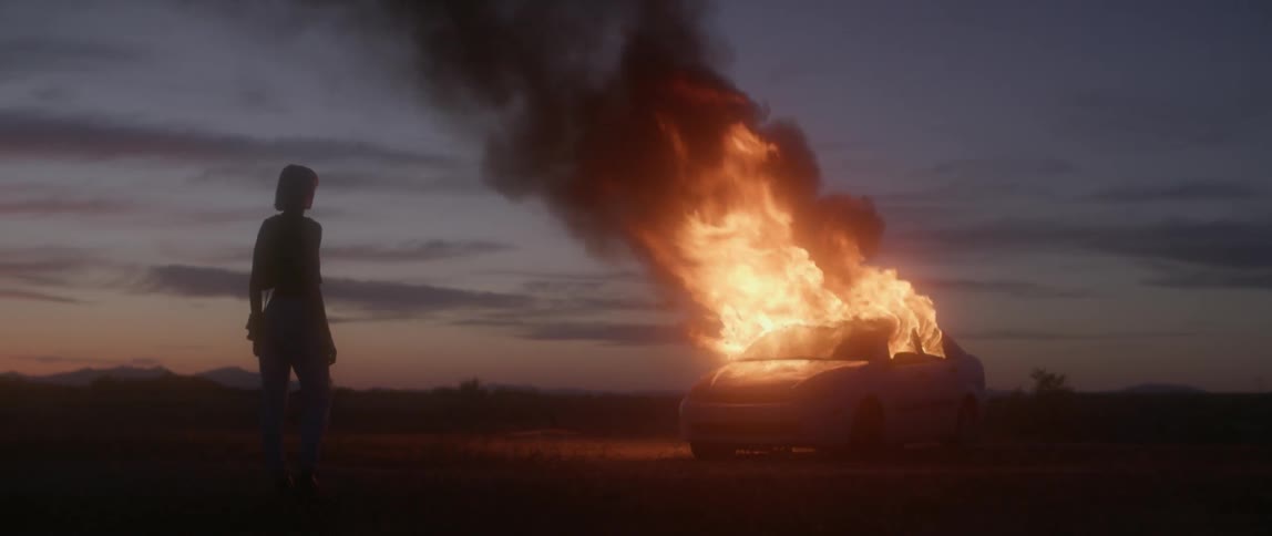 A woman watches as a car burns