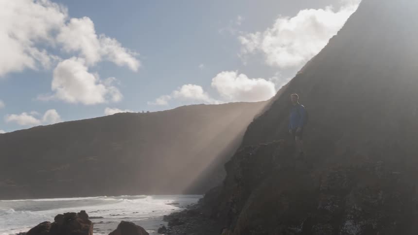 A man stands on a cliff by the shore
