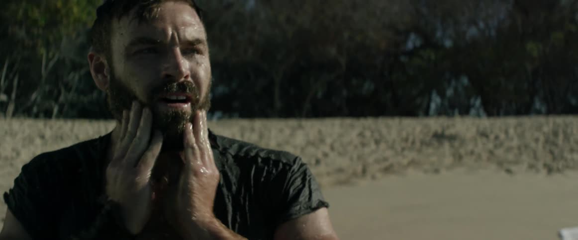 A man on a beach rubs his face and looks around