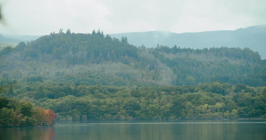 Water sits still in a lake in front of a hill