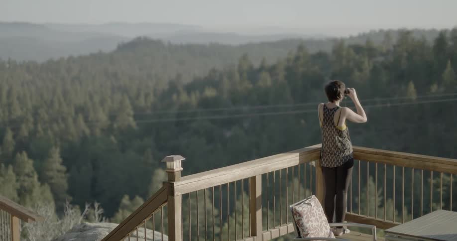 A woman takes a picture from a deck overlooking a forest