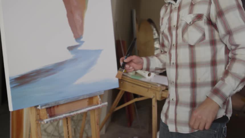 Man holding a brush paints on the canvas