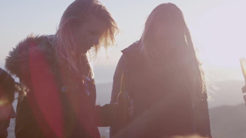 People holding beer bottles celebrate as the sun sets