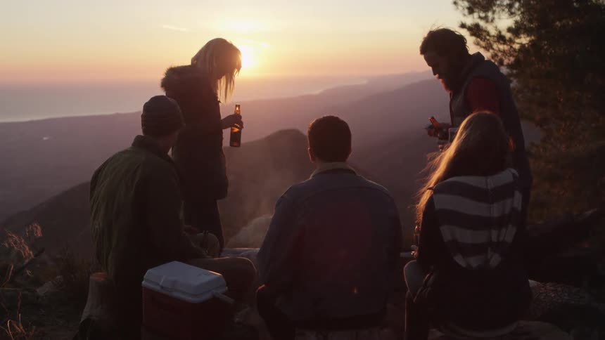 People sit on a high point overlooking a mountain range at sunset