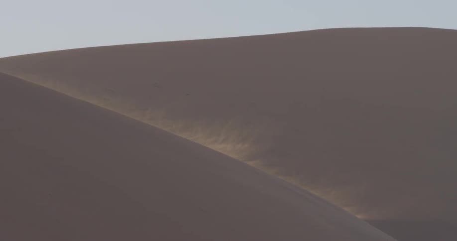The tall sand dune is blowing sand down