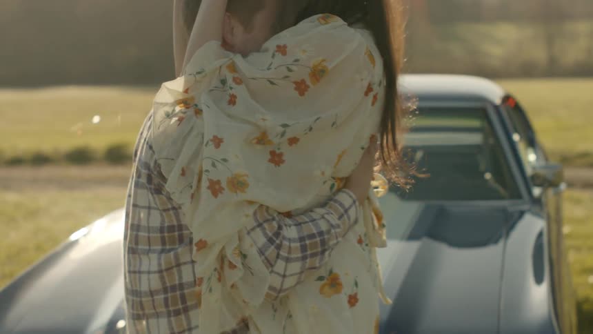 A man and woman hug in a rural field on a sunny day