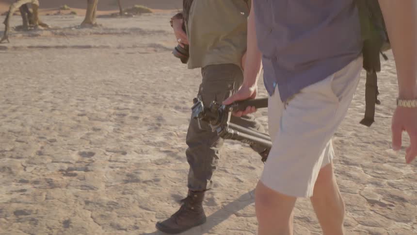 Two photographers walk on the cracked packed sand of a desert