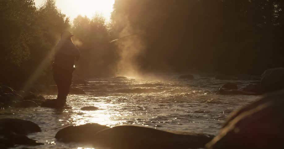 A fisherman is casting his line into a river at dawn