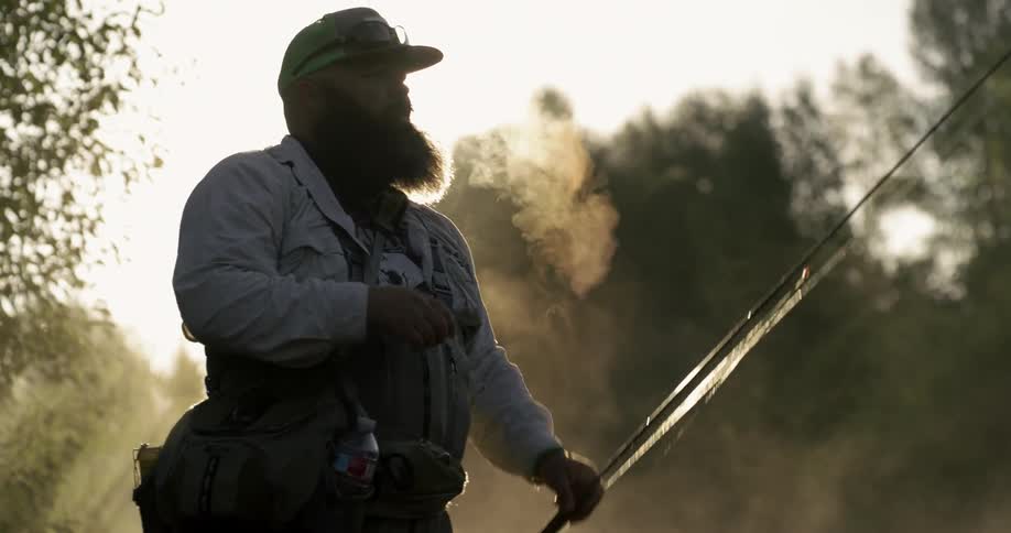 A man slowly lifts their fishing pole as he wipes his brow