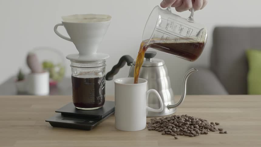 Two coffee pots shown, as a mug is filled with a brown liquid from a glass beaker