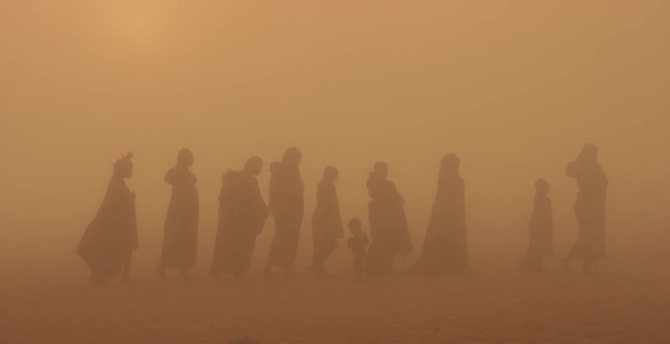 A tribe of women and children are walking during a sandstorm